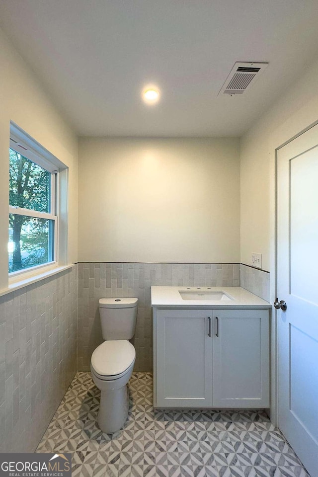 bathroom featuring vanity, toilet, and tile walls