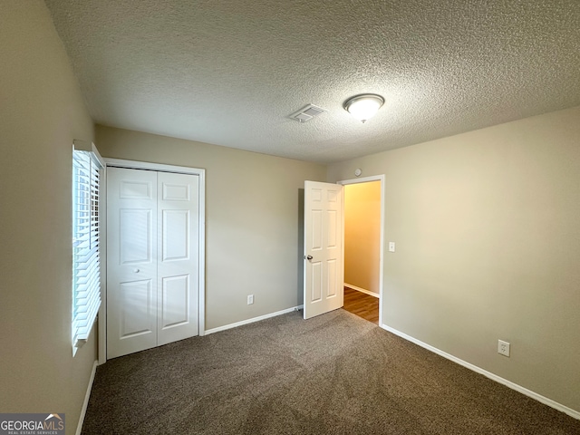 unfurnished bedroom with dark colored carpet, a textured ceiling, and a closet