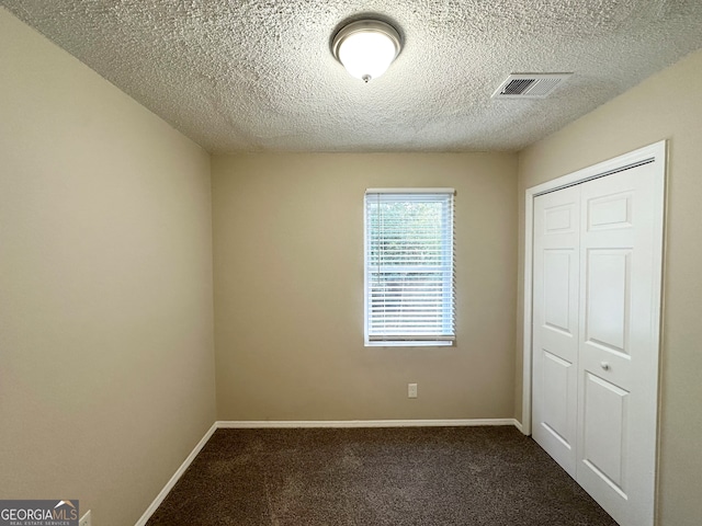 unfurnished bedroom featuring a textured ceiling, dark carpet, and a closet