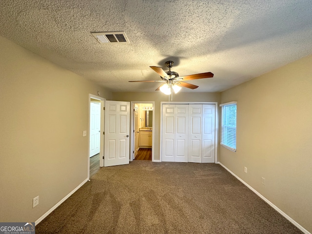 unfurnished bedroom with dark carpet, ceiling fan, a textured ceiling, connected bathroom, and a closet