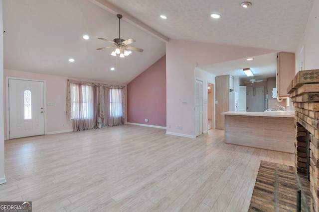 unfurnished living room with a fireplace, lofted ceiling with beams, light hardwood / wood-style floors, and ceiling fan