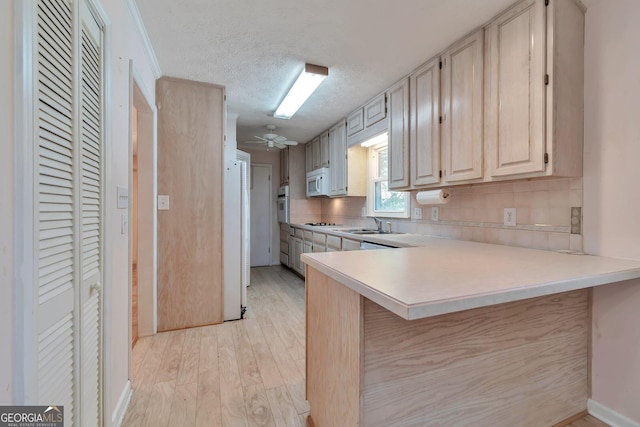 kitchen with white appliances, a breakfast bar area, light hardwood / wood-style floors, a textured ceiling, and kitchen peninsula