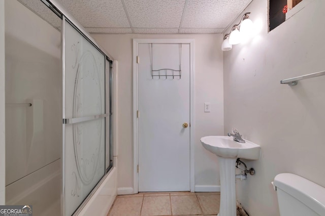 bathroom featuring a drop ceiling, combined bath / shower with glass door, tile patterned floors, and toilet