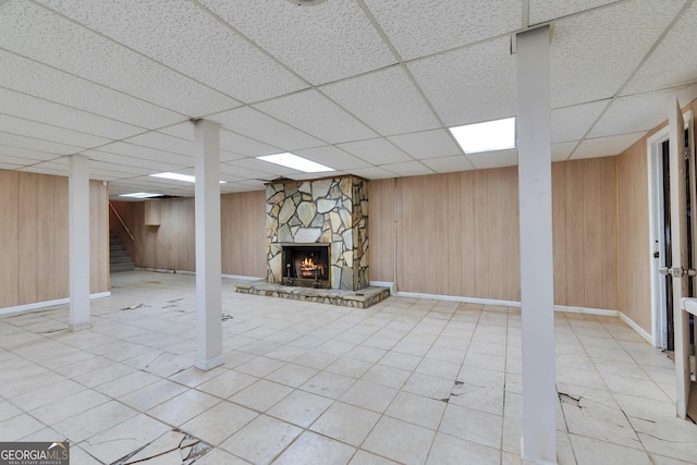 basement featuring a drop ceiling, a fireplace, and wooden walls