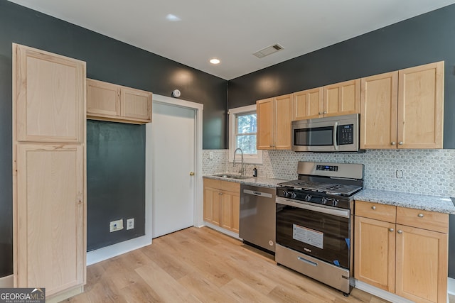 kitchen with sink, light wood-type flooring, light stone countertops, light brown cabinetry, and appliances with stainless steel finishes