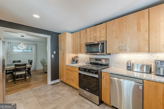 kitchen featuring light wood-type flooring, tasteful backsplash, light stone counters, stainless steel appliances, and hanging light fixtures