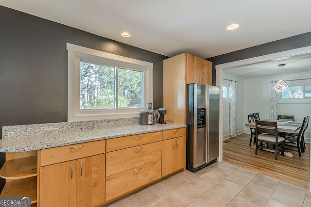 kitchen with hanging light fixtures, light hardwood / wood-style flooring, stainless steel fridge, light stone counters, and kitchen peninsula