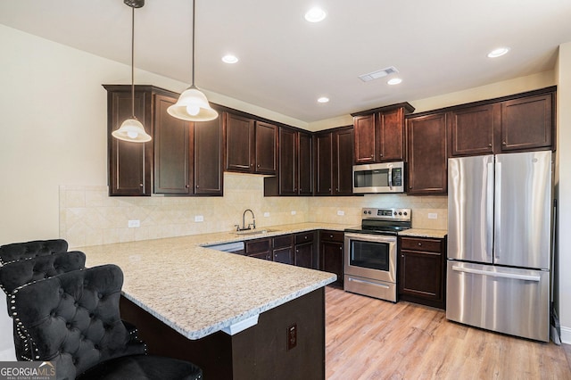 kitchen with a kitchen breakfast bar, light hardwood / wood-style flooring, decorative light fixtures, kitchen peninsula, and stainless steel appliances