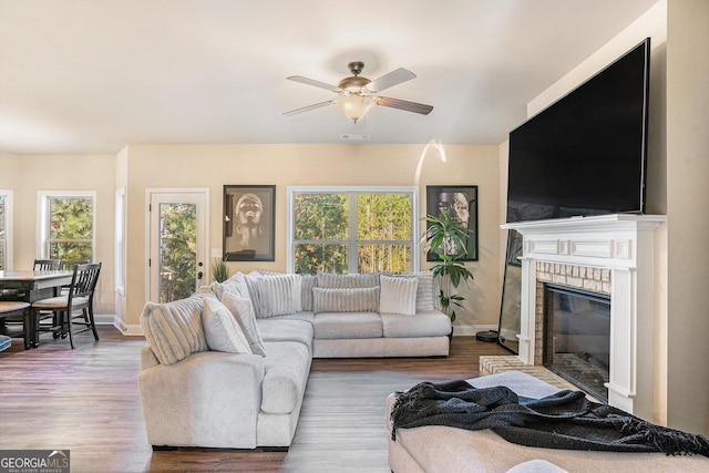 living room with ceiling fan, dark wood-type flooring, a wealth of natural light, and a brick fireplace