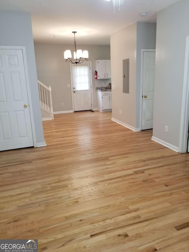 unfurnished living room featuring a notable chandelier, light wood-type flooring, and electric panel