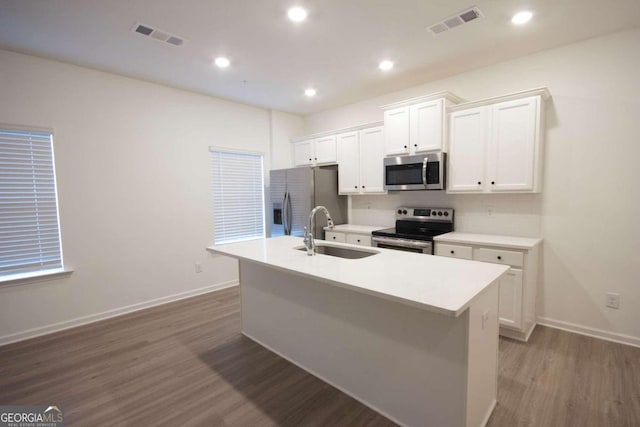 kitchen with appliances with stainless steel finishes, sink, white cabinets, light hardwood / wood-style floors, and an island with sink