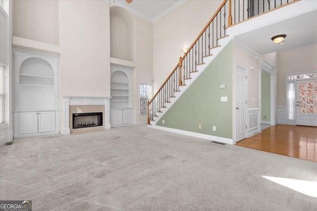 unfurnished living room featuring crown molding, a wealth of natural light, built in features, and carpet flooring