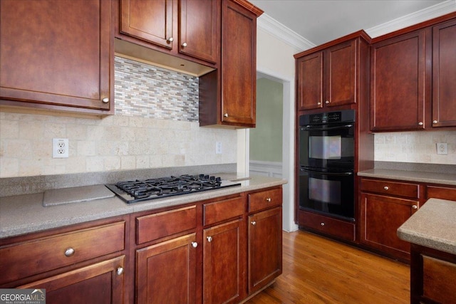 kitchen with black double oven, ornamental molding, stainless steel gas cooktop, and decorative backsplash