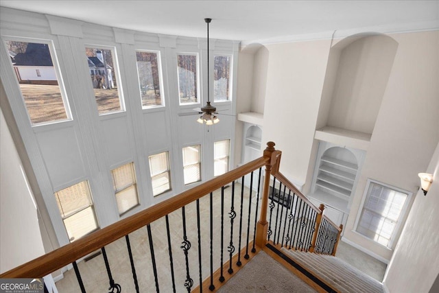 staircase with built in shelves, ornamental molding, ceiling fan, and carpet flooring