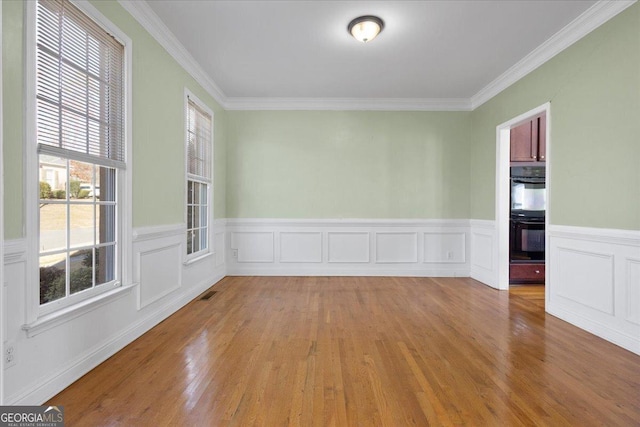 empty room with crown molding, plenty of natural light, and light hardwood / wood-style floors