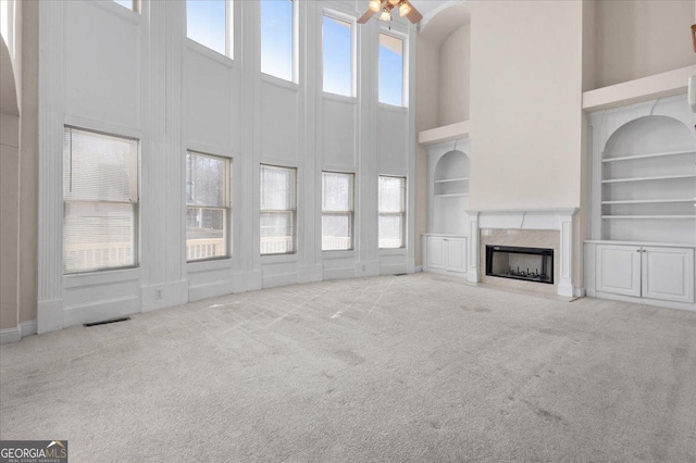 unfurnished living room featuring a towering ceiling, a high end fireplace, light carpet, and built in features