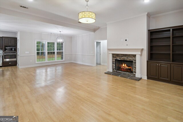 unfurnished living room with light hardwood / wood-style floors, a stone fireplace, ornamental molding, and a chandelier