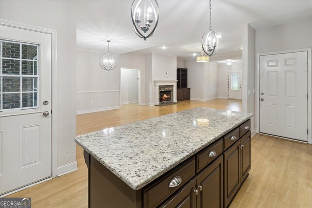 kitchen with a center island, a stone fireplace, hanging light fixtures, light hardwood / wood-style floors, and dark brown cabinetry