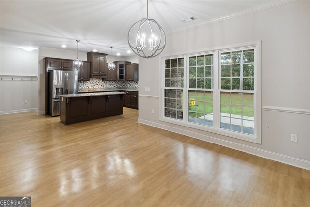 kitchen featuring stainless steel refrigerator with ice dispenser, backsplash, pendant lighting, dark brown cabinets, and a kitchen island