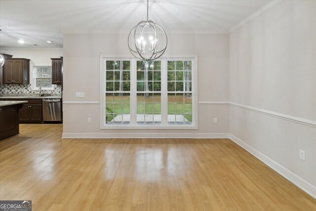 unfurnished dining area with a healthy amount of sunlight, crown molding, and an inviting chandelier