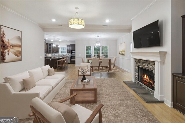 living room with light hardwood / wood-style floors, a stone fireplace, and ornamental molding