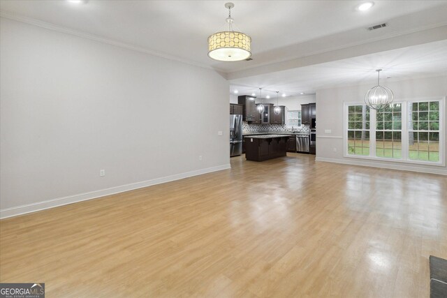 unfurnished living room with a chandelier, light hardwood / wood-style flooring, and crown molding