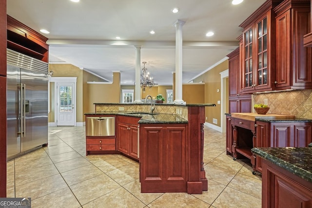 kitchen featuring tasteful backsplash, dark stone counters, sink, an inviting chandelier, and an island with sink