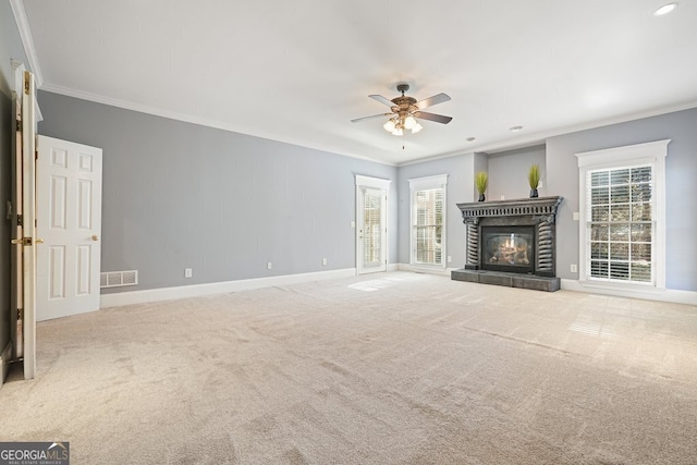 unfurnished living room featuring a tiled fireplace, crown molding, plenty of natural light, and light colored carpet