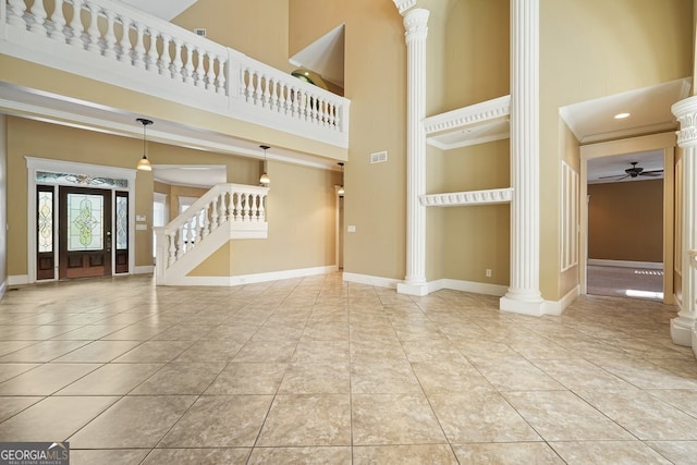 unfurnished living room with ornate columns, ceiling fan, a towering ceiling, and ornamental molding