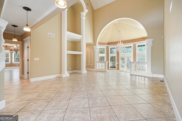 tiled empty room with a chandelier, crown molding, a high ceiling, and decorative columns