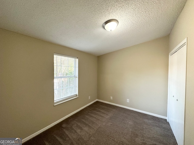 unfurnished room featuring dark carpet and a textured ceiling