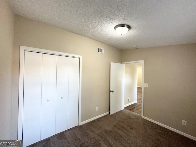 unfurnished bedroom with a textured ceiling, dark carpet, and a closet