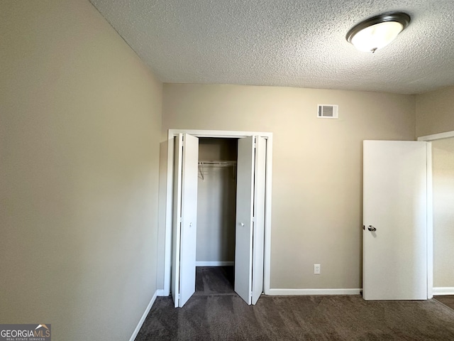 unfurnished bedroom featuring dark colored carpet, a textured ceiling, and a closet