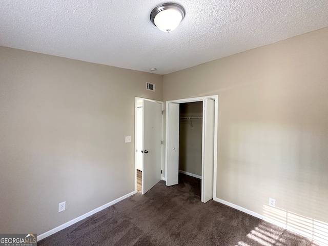 unfurnished bedroom with dark colored carpet, a textured ceiling, and a closet