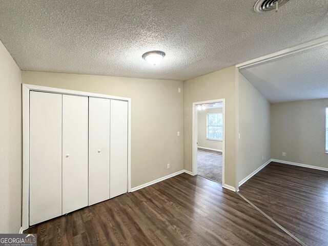 unfurnished bedroom featuring a textured ceiling, dark hardwood / wood-style flooring, a closet, and lofted ceiling