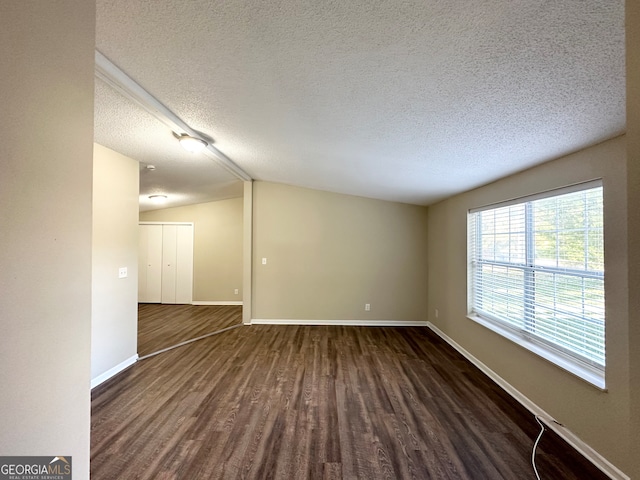 empty room featuring lofted ceiling, a textured ceiling, and dark wood-type flooring