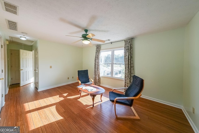 sitting room featuring ceiling fan, light hardwood / wood-style flooring, and a textured ceiling