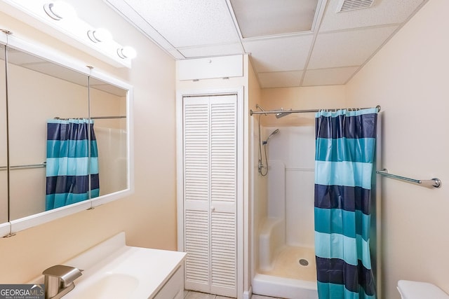 bathroom with toilet, a paneled ceiling, vanity, and walk in shower