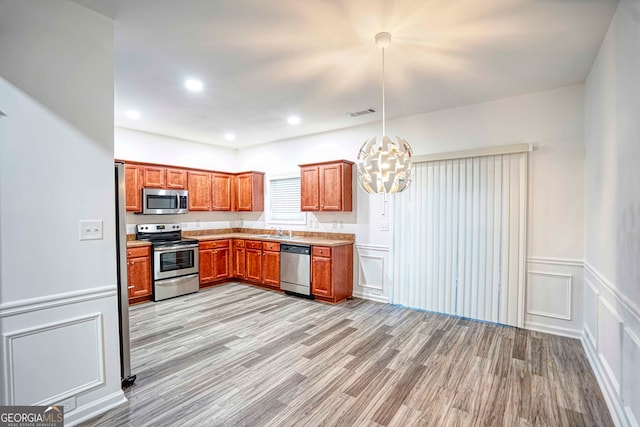 kitchen featuring sink, an inviting chandelier, light hardwood / wood-style floors, decorative light fixtures, and appliances with stainless steel finishes