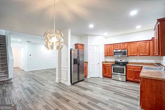 kitchen with stainless steel appliances, sink, pendant lighting, a notable chandelier, and light hardwood / wood-style floors