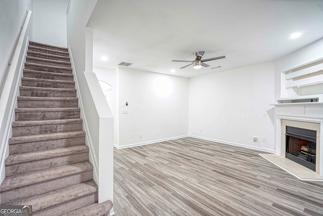 unfurnished living room with hardwood / wood-style flooring, ceiling fan, and a tiled fireplace