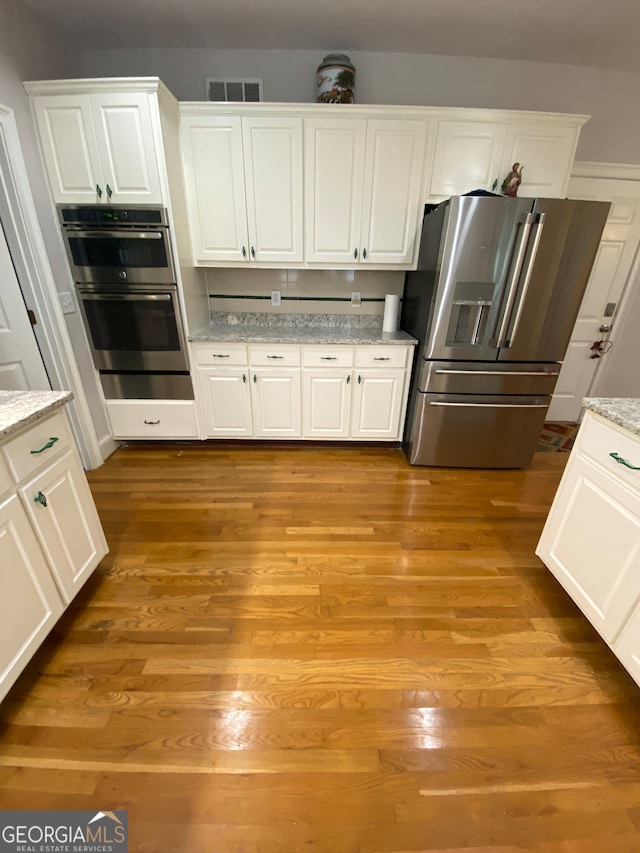 kitchen featuring light stone countertops, white cabinetry, light hardwood / wood-style flooring, and stainless steel appliances