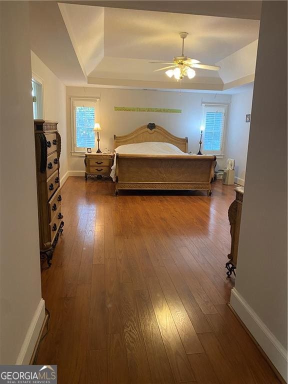 bedroom featuring hardwood / wood-style flooring, a raised ceiling, and ceiling fan