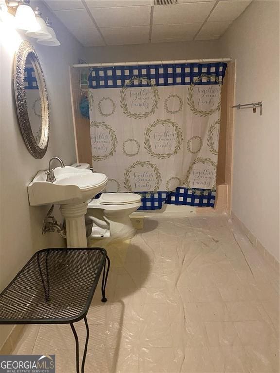 bathroom featuring a drop ceiling, curtained shower, and toilet