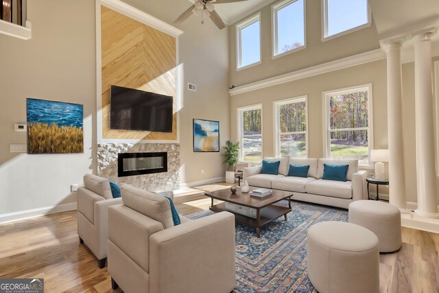 living room with ornate columns, ceiling fan, light hardwood / wood-style flooring, a fireplace, and a high ceiling