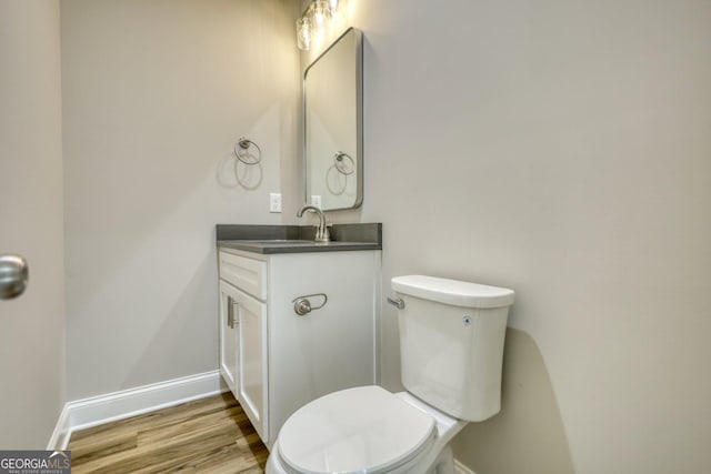 half bath featuring toilet, baseboards, wood finished floors, and vanity