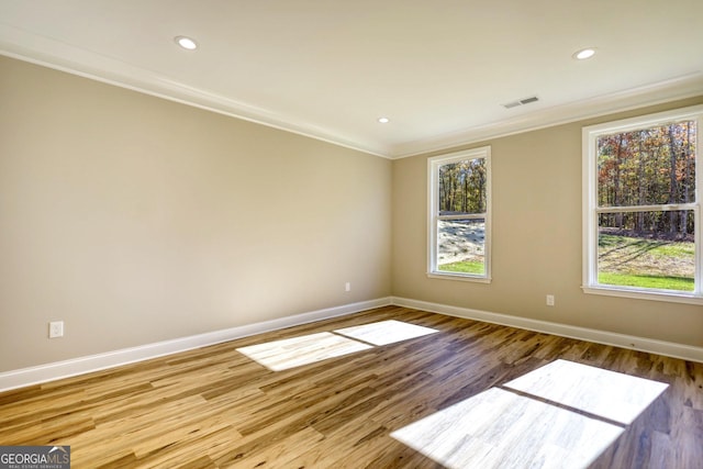 empty room with plenty of natural light, visible vents, crown molding, and wood finished floors