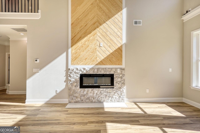 unfurnished living room featuring wood finished floors, a towering ceiling, visible vents, and baseboards