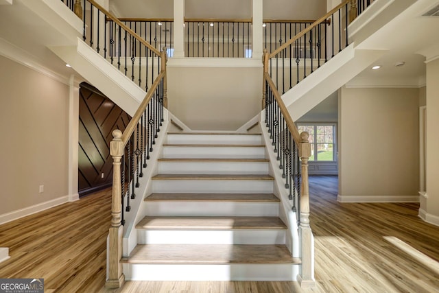 staircase with a towering ceiling, baseboards, and wood finished floors