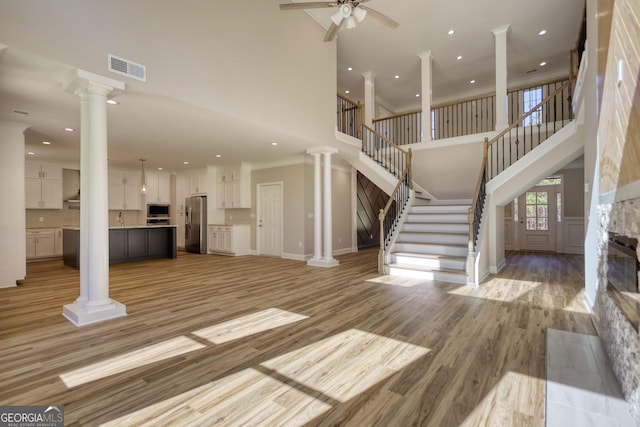 unfurnished living room featuring decorative columns, visible vents, stairway, light wood-style floors, and ceiling fan